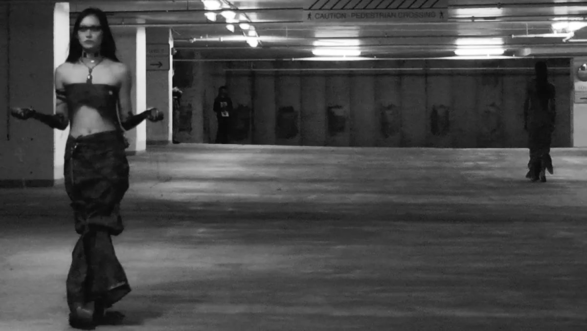 Black and white: a model with her arms held out walks the length of an empty parking level.