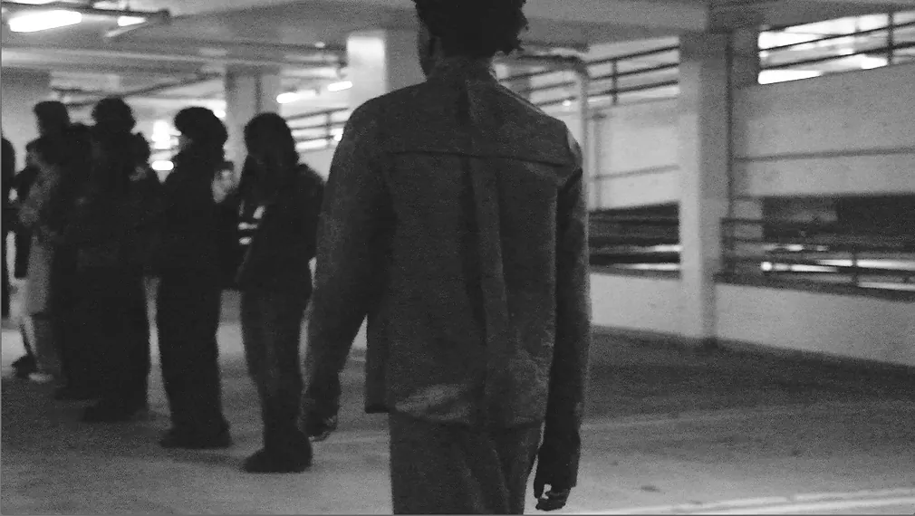Models waiting in a line in the garage as another walks past in a denim jacket.