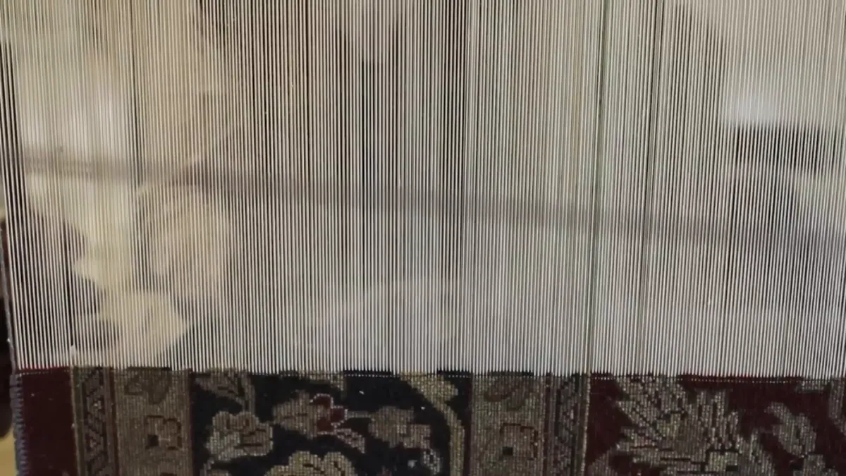 A hand-knotted rug in progress on the loom, the warp threads rising above it.
