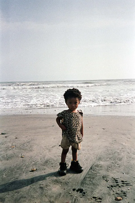 A small child in a leopard-print top standing on the wet sand.