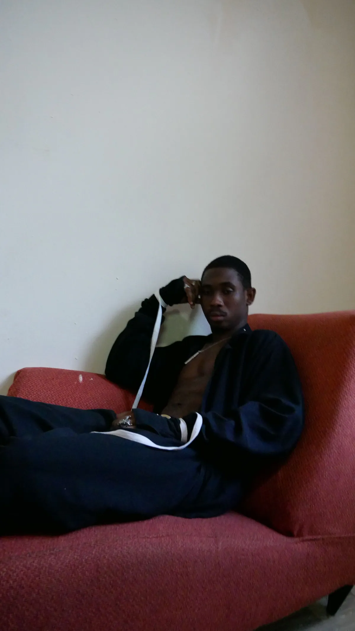 A man in a dark tracksuit lounging on a red sofa, shown twice as a mirror image.