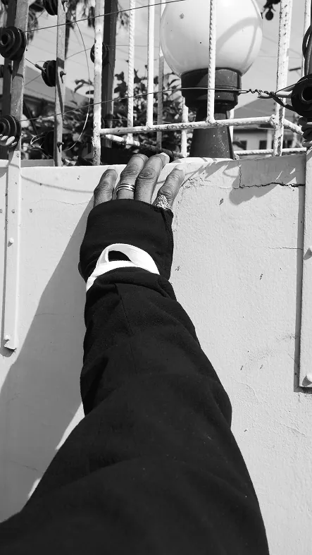 Black and white: an arm in a black sleeve with a white-lined cuff, the hand resting on top of a white wall beneath a street lamp.