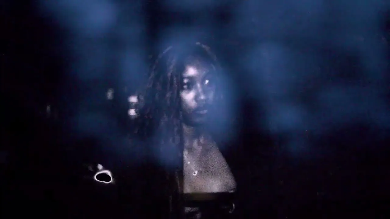 Still from the WAAR film: a model’s face, half lit, through blue haze.