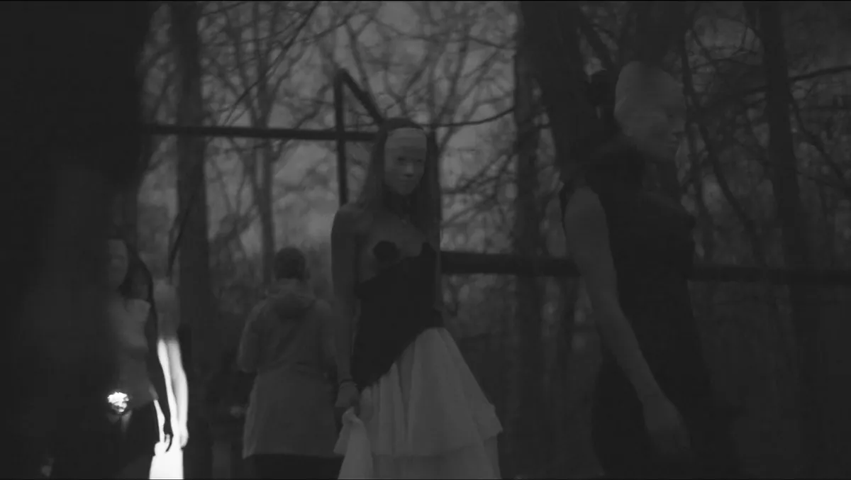 Masked models moving between bare trees at dusk during the show.