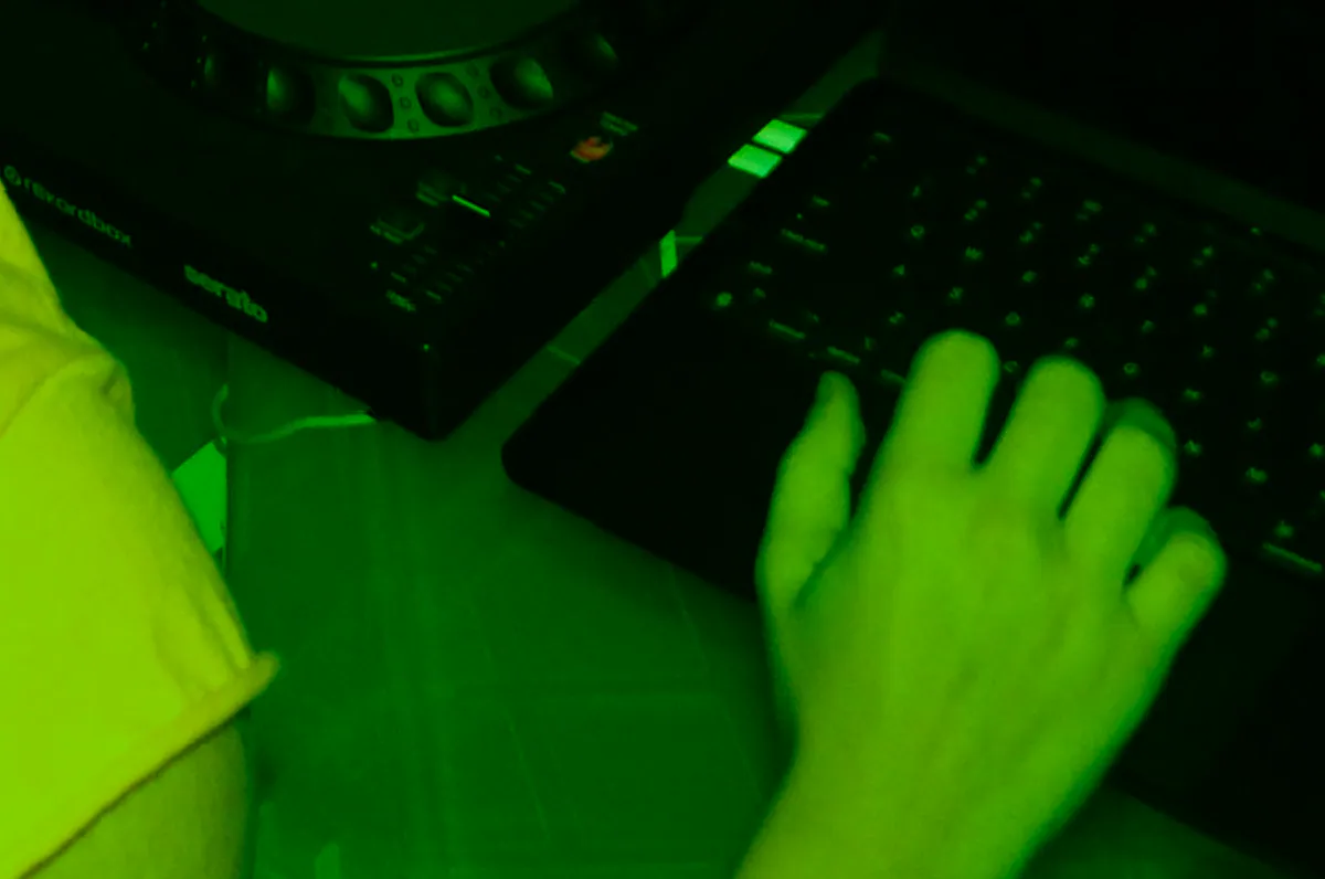 A hand on a synth keyboard under green light.