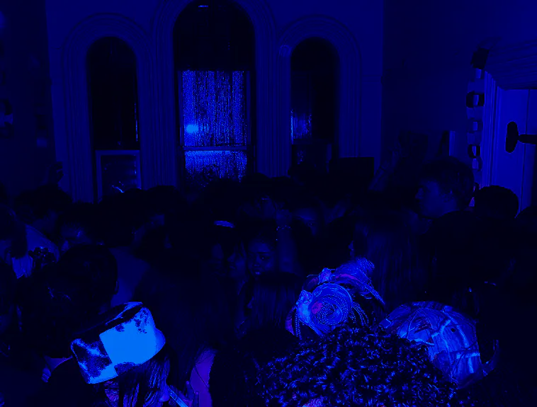 A room in deep blue light, people gathered beneath arched windows.