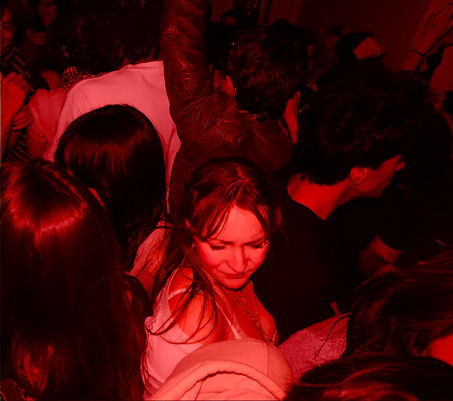A crowd under red light, one woman looking down and smiling.